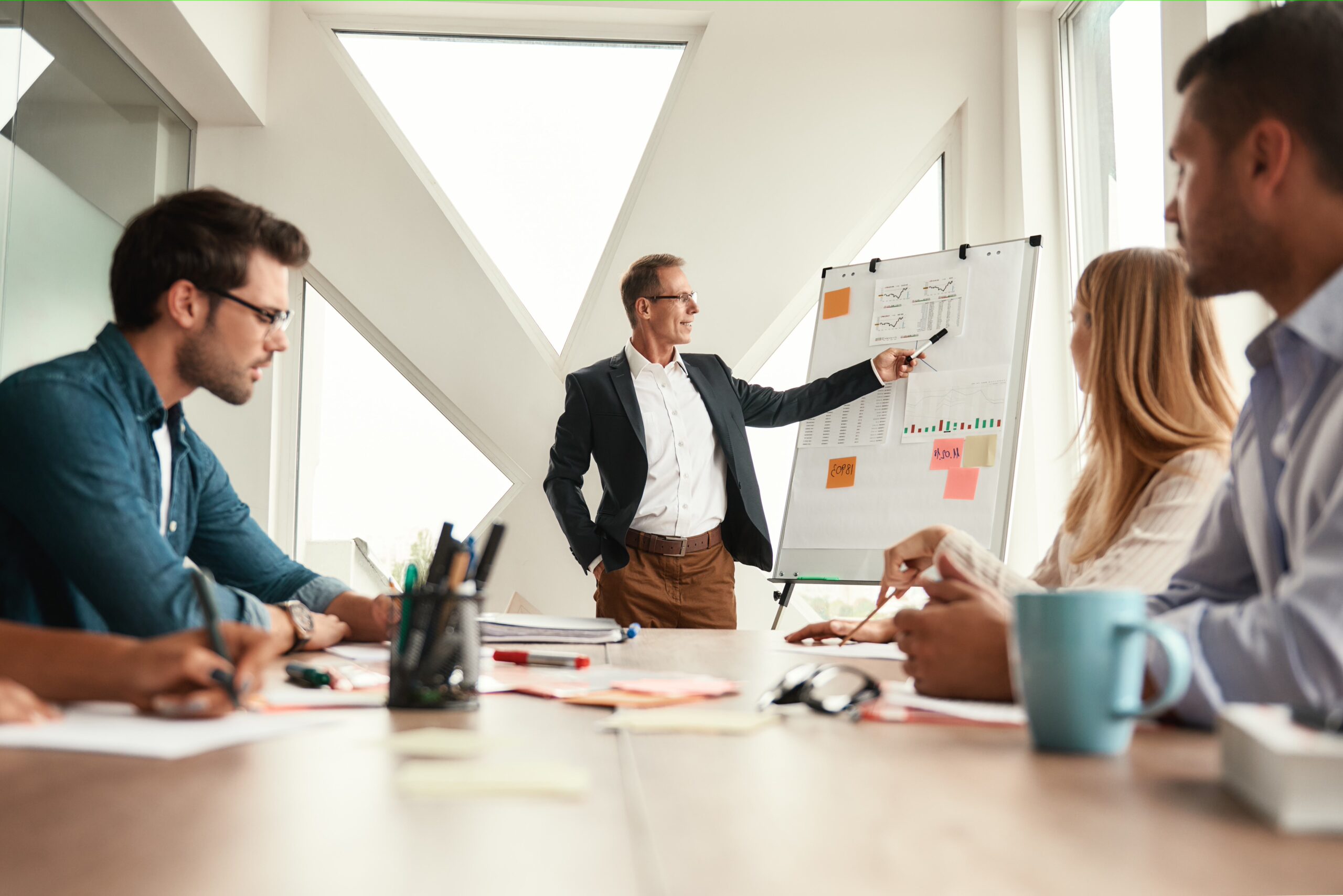 Fresh ideas. Mature businessman standing near whiteboard and explaining something to his young colleagues. Teamwork. Meeting